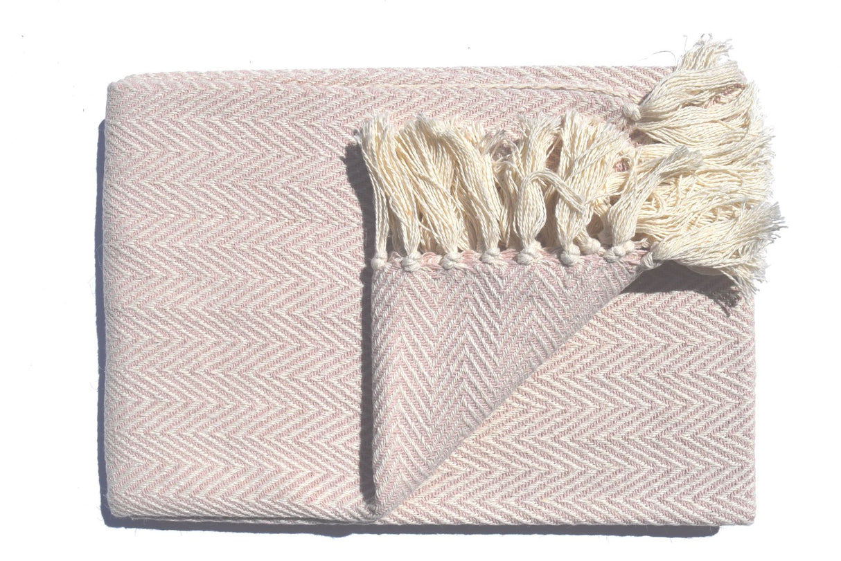 A soft, lightweight Skye Throw with a herringbone weave and coloured tassels draped over a sofa