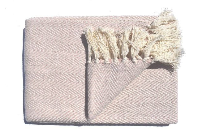 A soft, lightweight Skye Throw with a herringbone weave and coloured tassels draped over a sofa