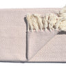 A soft, lightweight Skye Throw with a herringbone weave and coloured tassels draped over a sofa