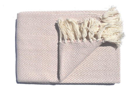 A soft, lightweight Skye Throw with a herringbone weave and coloured tassels draped over a sofa