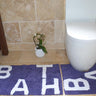 Set of two natural cotton bath mats, including a large bath mat and matching pedestal mat, both displaying the word bath in stylish lettering