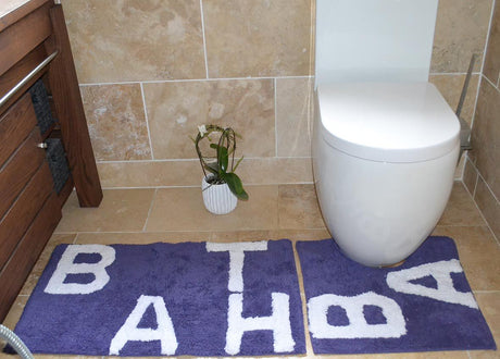 Set of two natural cotton bath mats, including a large bath mat and matching pedestal mat, both displaying the word bath in stylish lettering