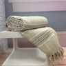 Stitch Stripe Throw casually folded on a chair, showcasing its warm cotton texture and decorative tassels